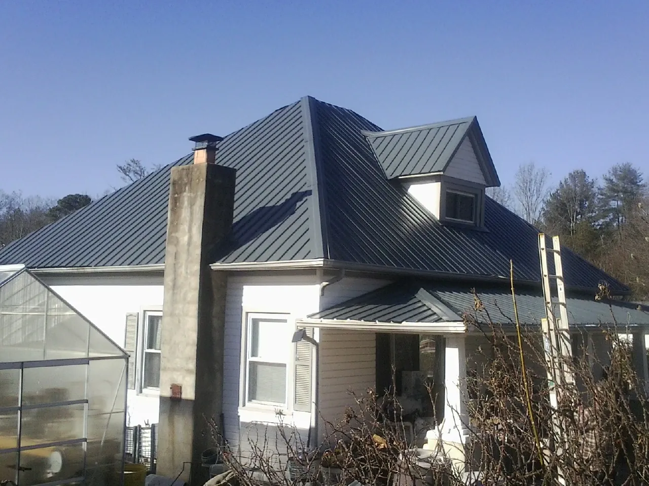 Dark blue standing seam metal roof on a white farmhouse with dormer — Slate & Tile Roof Repair by Roofing Brothers in Batesburg