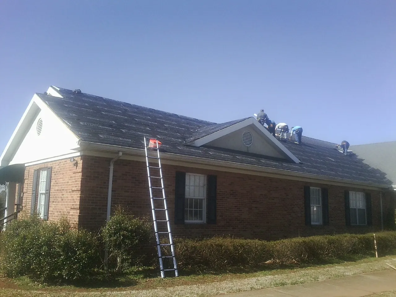 Crew tearing shingles off a brick ranch roof with a ladder set — Emergency Roof Repair work by our crew in Batesburg