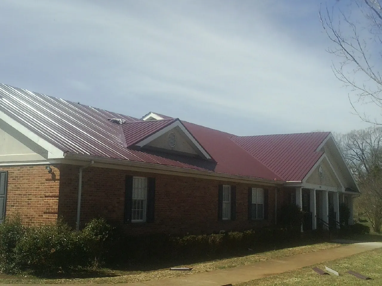 Red metal roof with gabled entries on a long brick building, from a Hail Damage Roof Repair job in Batesburg