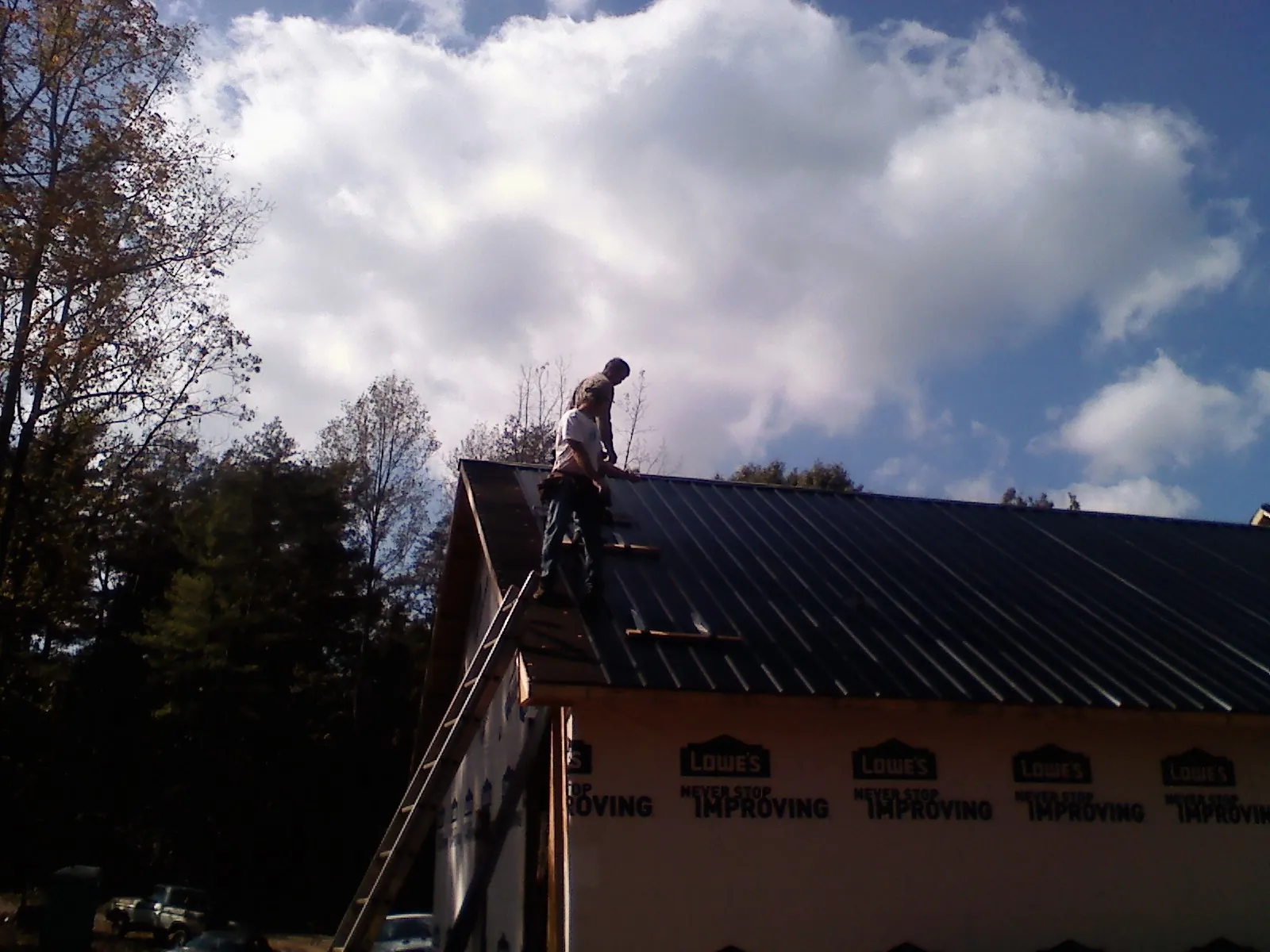 Roofer fastening dark metal panels high against a cloudy sky, from a Roof Inspection job in Batesburg