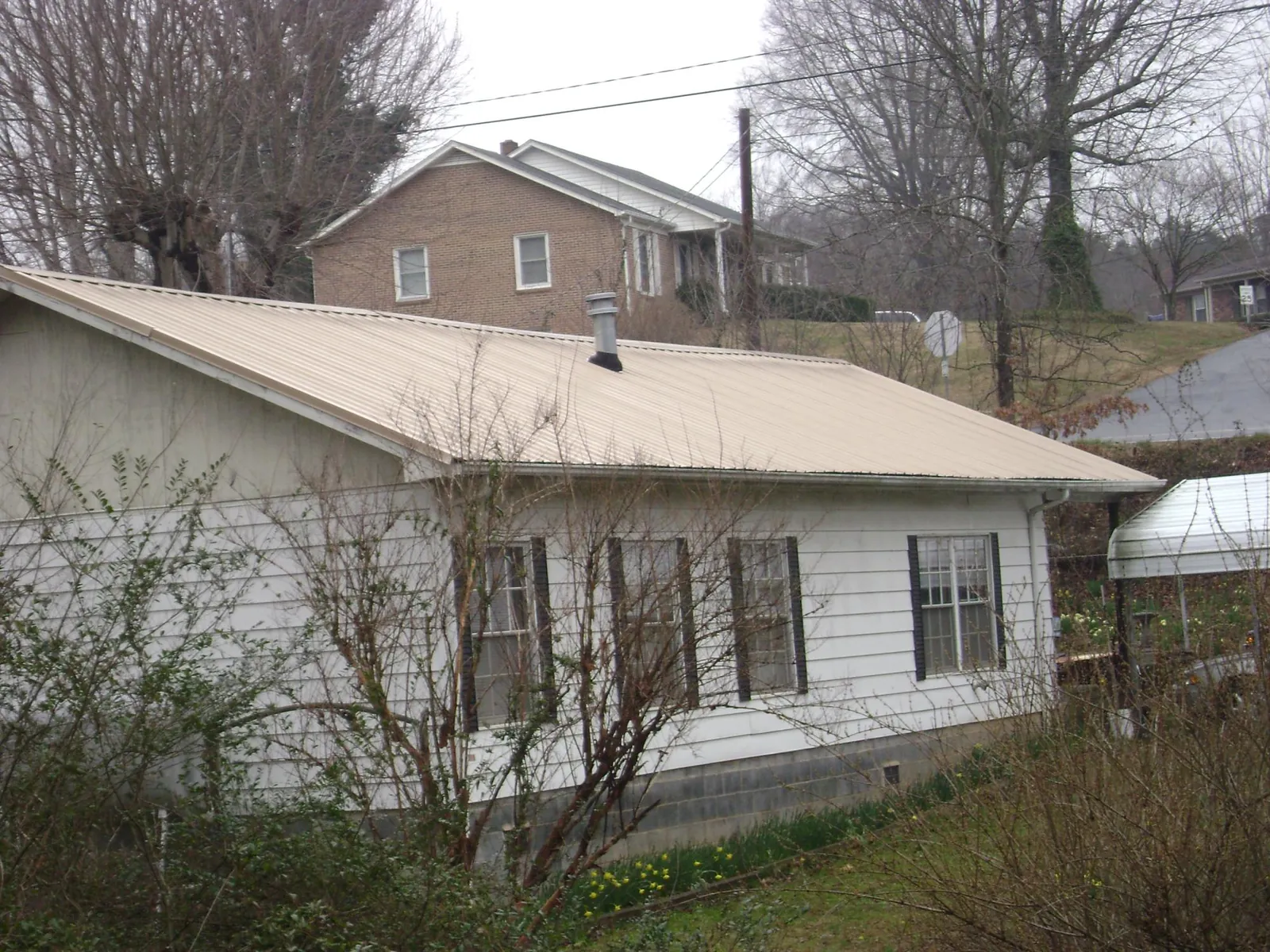 Tan metal roof on a white sided house set into a hillside — Commercial Roofing by Roofing Brothers in Batesburg